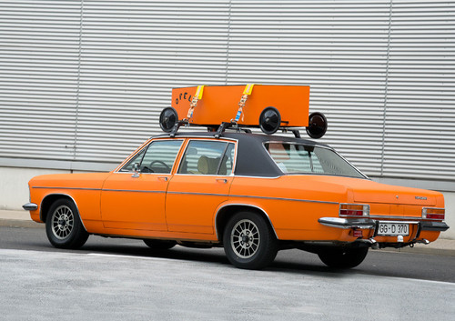 Opel Diplomat B mit 2,8-Liter-Reihensechszylinder und Automatik-Getriebe, orange-farbig foliert und mit Seifenkiste auf dem Dach für den Einsatz bei der Youngtimer-Rallye Creme 21.