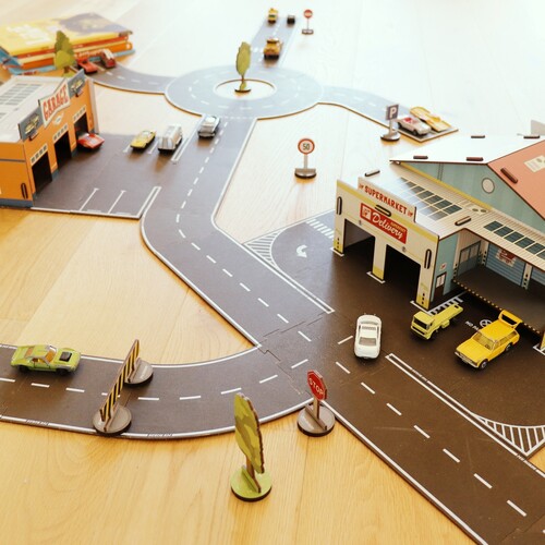 Spielzeugstraßensystem „My Roads“ aus Holz mit Kfz-Werkstatt (links), Kreisverkehr (oben) und Supermarkt (rechts die Rückseite). 
