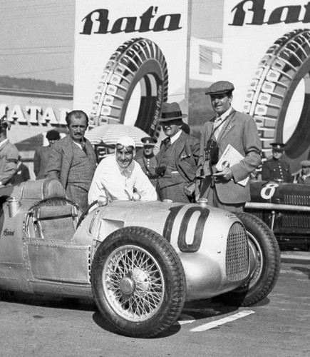 Hans Stuck in dem Auto-Union Rennwagen beim Großen Preis von Brünn 1934 auf dem Masaryk-Ring. Links neben Hans Stuck steht Ferdinand Porsche.