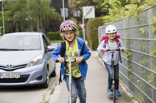 Kinder auf Roller mit Helm.