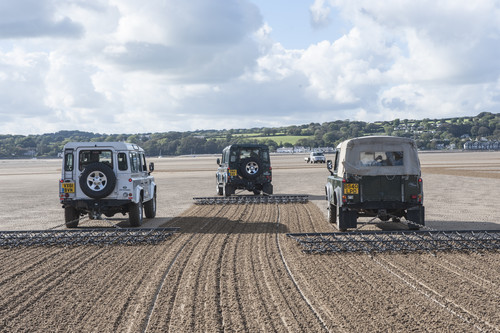 Sechs Land Rover Defender unterschiedlicher Baujahre zeichneten den überdimensionalen Umriss des legendären Geländewagens in den Sand von Anglesey.